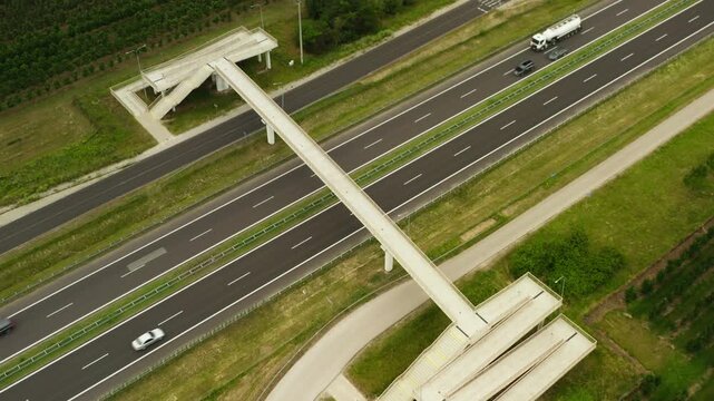 Concrete pedestrian overpass crosses a multi lane highway with active traffic. Modern asphalt road infrastructure connects rural areas for transport logistics and public safety on a summer day.