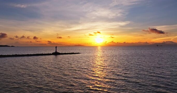 Aerial view of a golden sunrise over the calm sea with a lighthouse on the breakwater in Zhuhai, China