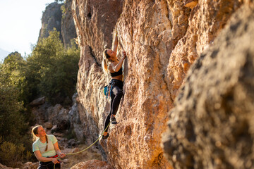 Fototapeta premium Young woman lead climbing, friend climber belaying. sport climbing in nature.