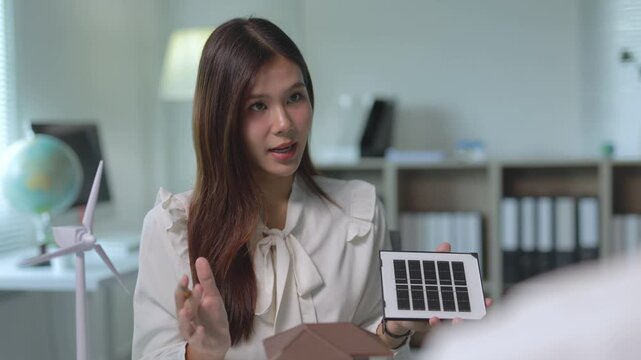 Young businesswoman discussing green energy solutions with a colleague. She presents a solar panel model for home installation
