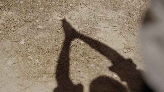 Human arm shadow reaches upward clasped hands. Blurred arm extends toward the shadow. Shadow forms a reaching gesture. Praying silhouette on desert ground. Religious moment