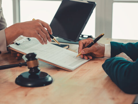 Lawyer holding pen and explaining legal contract terms on clipboard to client during consultation in law firm.