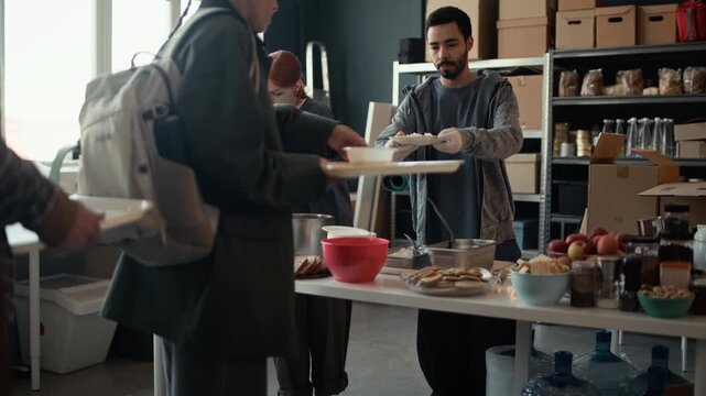 Young adult Caucasian woman and young adult Middle Eastern man volunteering at food bank, serving hot meals to people in need. Footage suits charity campaigns and social service promotions
