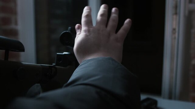 Cinematic over-the-shoulder footage of a masked sniper aiming a scoped rifle toward a window in a dark interior.