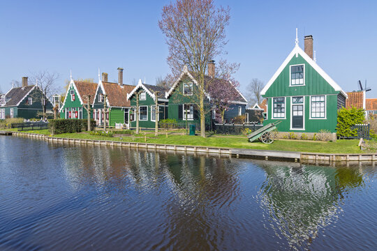 Zaandam, Netherlands: A row of historic green wooden residences with ornate gables reflecting in the calm canal water on a sunny day.