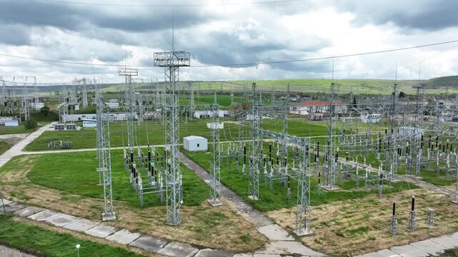 Aerial view of an electrical substation and high-voltage power lines with a wind farm on the horizon. Energy grid infrastructure, symbolizing the transition to renewable power.