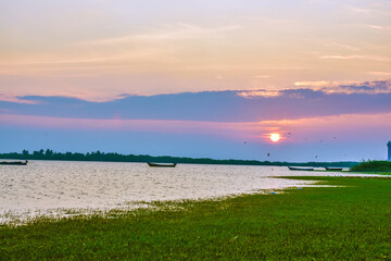Obraz premium Golden sunrise over a tranquil coastal lagoon with fishing boats, birds, and a distant lighthouse in Dhanushkodi, Tamil Nadu, India