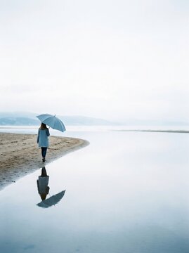 woman walking with umbrella on beach in moody weather