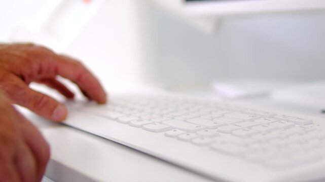 Male hand pressing key on white computer keyboard placed on clean office desk demonstrating everyday typing and modern workplace close up technology video