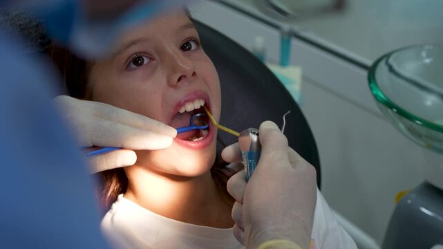 Dentist treating little girl teeth with dental drill and mirror in clinic close up.