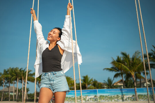 Happy woman celebrating freedom holding white shirt in the wind against blue sky at tropical beach