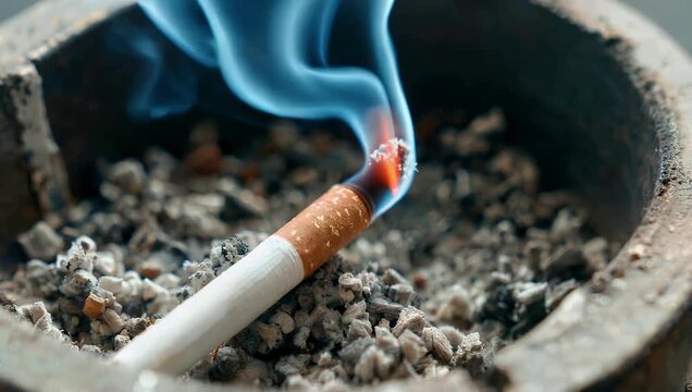 Moody and highly atmospheric 4K macro footage of a lit tobacco cigarette resting in a glass receptacle capturing elegant wisps of blue vapor rising upward with dramatic shadow play ideal for