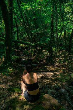 Woman Sitting by Mossy Forest Stream &ndash; Peaceful Nature Retreat in Green Woods