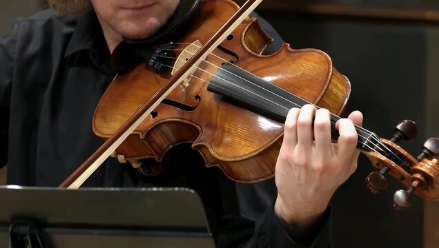 A highly expressive close up 4K performance video capturing the hands of a professional violinist playing a wooden violin showing fast precise finger movements against a black background
