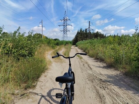 POV shot of a bicycle handlebar on a sandy countryside road leading to power lines