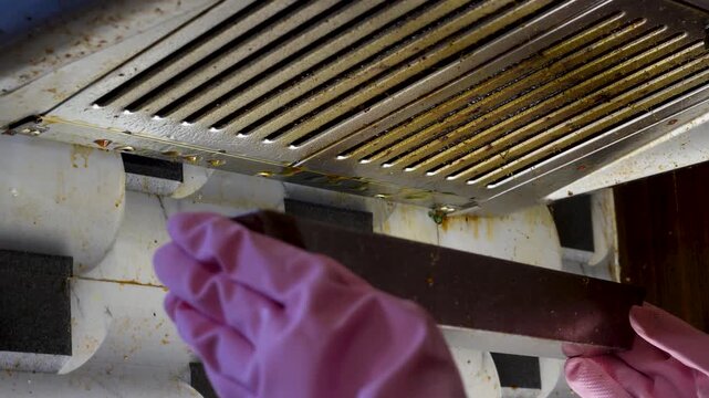 Gloved hand removing dirty cooker hood filter for cleaning or service. Grease and grime buildup requires regular maintenance for modern kitchen appliance hygiene.