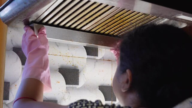 Gloved hand removing dirty cooker hood filter for cleaning or service. Grease and grime buildup requires regular maintenance for modern kitchen appliance hygiene.