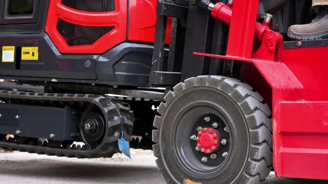 Close-up shot of a red forklift lifting a mini excavator during a warehouse logistics operation. High quality 4k footage