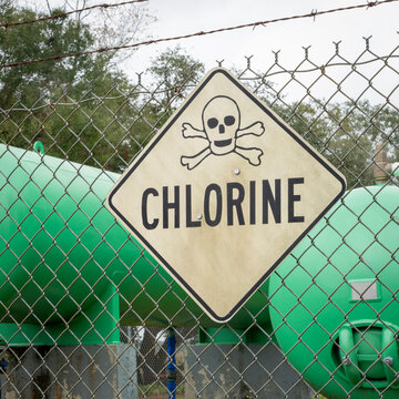industrial chlorine gas tanks behind a fence with a warning sign