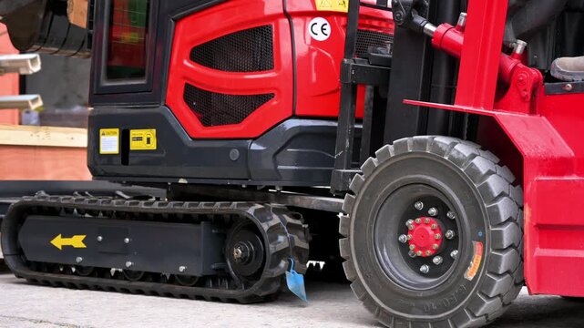 Close-up shot of a red forklift lifting a mini excavator during a warehouse logistics operation. High quality 4k footage
