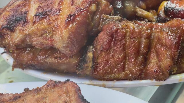 Grilled pork chops and roasted chicken displayed on a street food stall, seen through a glass cabinet