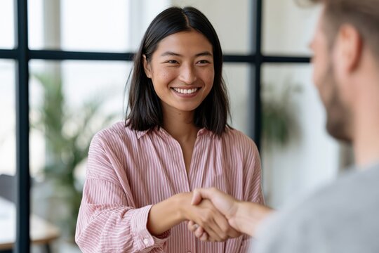 Asian professional woman smiling while shaking hands with a colleague in a contemporary office for corporate banner and website background