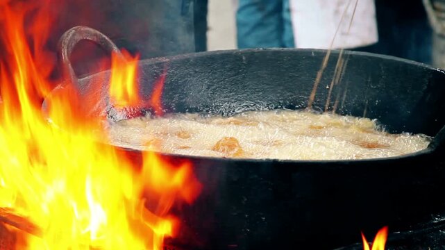 Traditional Deep Frying chicharron  in Cast Iron Cauldron over Open Fire Flames