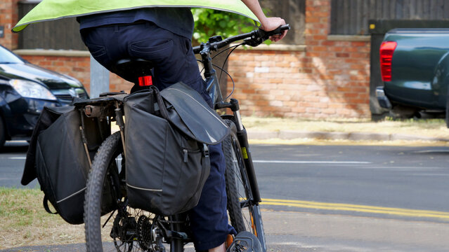 Cyclist with pannier bags riding bicycle on city street, rear view of commuter in high visibility vest cycling on road with bike saddlebags