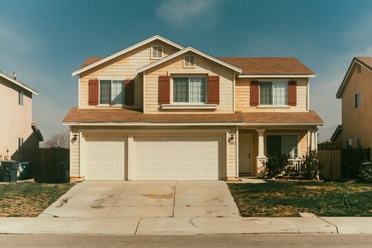 Two story craftsman house with a three car garage and concrete driveway under a blue sky for residential real estate and suburban living