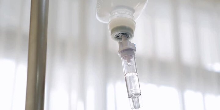 A hospital room's intravenous infusion drip bag suspends medically necessary fluids, slowly dripping medication into a patient's system via an attached tube during treatment or recovery