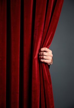 Red velvet stage curtain being pulled aside by a single hand, featuring soft plush texture and a mysterious theater atmosphere for premiere and performance advertising
