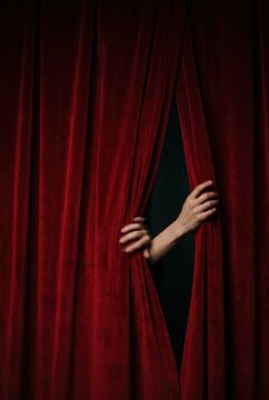 Red velvet stage curtains filling the frame as hands emerge to part the fabric for a theatrical performance, suspenseful premiere reveal imagery with copy space