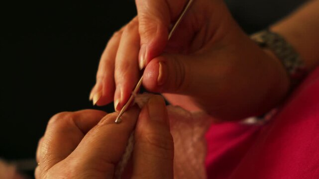 Woman crocheting white yarn with warm light.
