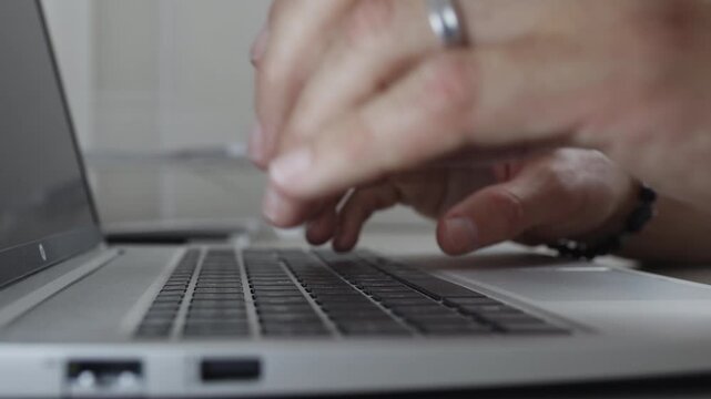 Close up side view of a man's hands rapidly typing on a laptop keyboard at a workplace