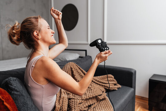 A stressed woman reacts to losing a match while playing video games in her cozy living room. She holds a gamepad and touches her head in frustration.