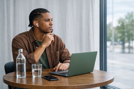 Thoughtful student man working at laptop in modern bright interior. Ai generative