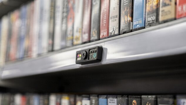 Smart shelves equipped with small sensors tracking media item quantities focused sensor array in center frame media cases subtly out of focus around.
