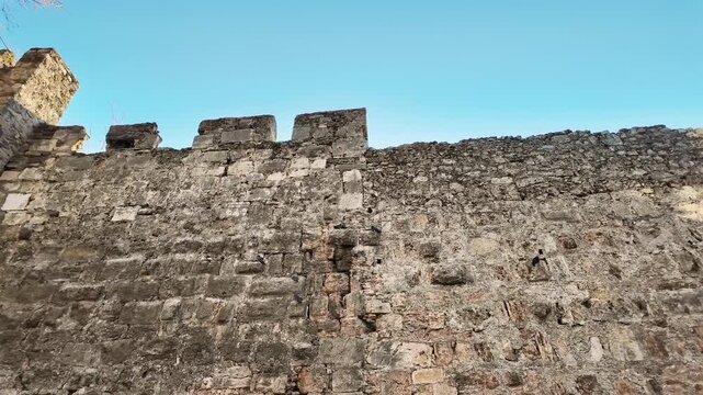 Weathered ancient stone fortress wall with battlements rising against clear blue sky in turkey.