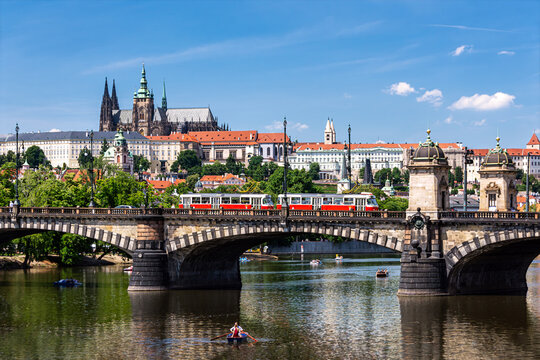 Prague Castle and St Vitus Cathedral overlook the Vltava River in a bright summer cityscape with bridges and historic architecture in the Czech capital.