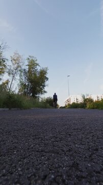 Rear view of a man with a backpack riding a bicycle on an asphalt path heading towards a modern residential area