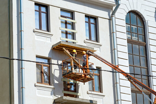 Workers removing shuttering panels from newly cast concrete balcony slab using aerial work platform, historic building facade restoration. Dismantling temporary wooden formwork. Balcony restoration