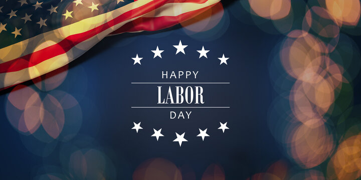 The wrinkled flag of the USA draped onto a flat dark blue surface with a bokeh light overlay and the text "Happy Labor Day"