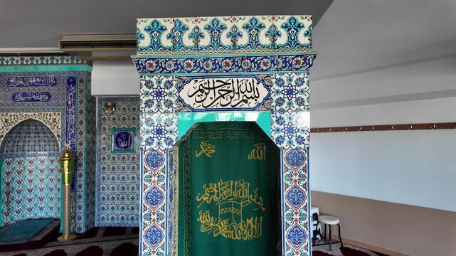 Detailed look at mosque interior showing beautiful minbar and mihrab decorated with classic blue Iznik style floral tiles and elegant Arabic calligraphy
