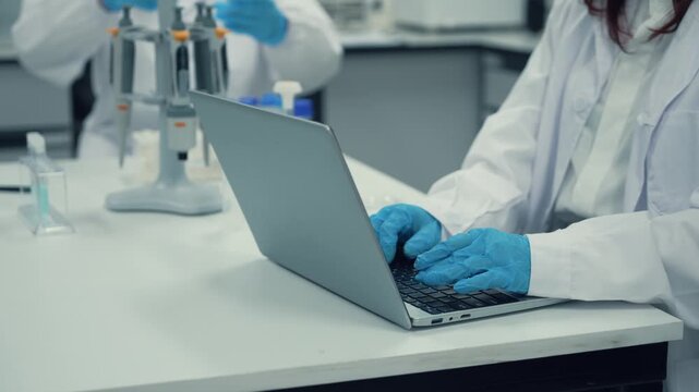 Scientist wearing lab coat and gloves working on a laptop computer keyboard in a modern laboratory