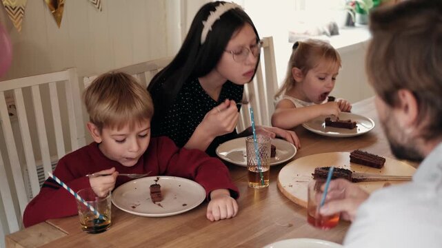 Children enjoying birthday cake with father at home party table. Happy dad eating sweet chocolate dessert with teenage girl, little boy and toddler daughter. Multi Child Family. Authentic Birthday