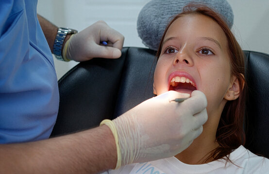 Close up of male dentist examining little girl teeth with probe under dental light