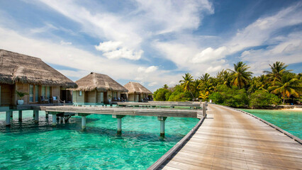 Fototapeta premium A serene tropical resort with thatched huts and a wooden walkway over crystal-clear waters