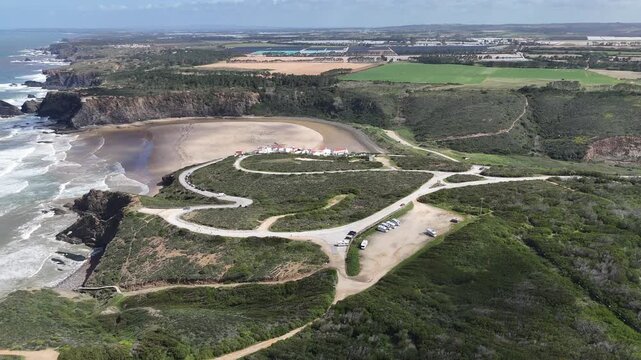 An aerial drone push in shot revealing the Praia de Odeceixe with rugged coastline and a sandy beach in Portugal. Lush green hills meet the Atlantic Ocean.