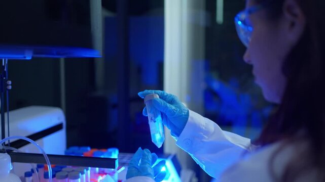 Female scientist working with test tube in a laboratory under blue ultraviolet light for DNA analysis or vaccine research