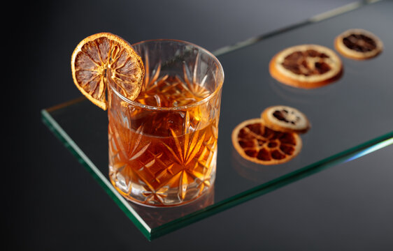 Old-fashioned cocktail with ice and a dried orange slice.